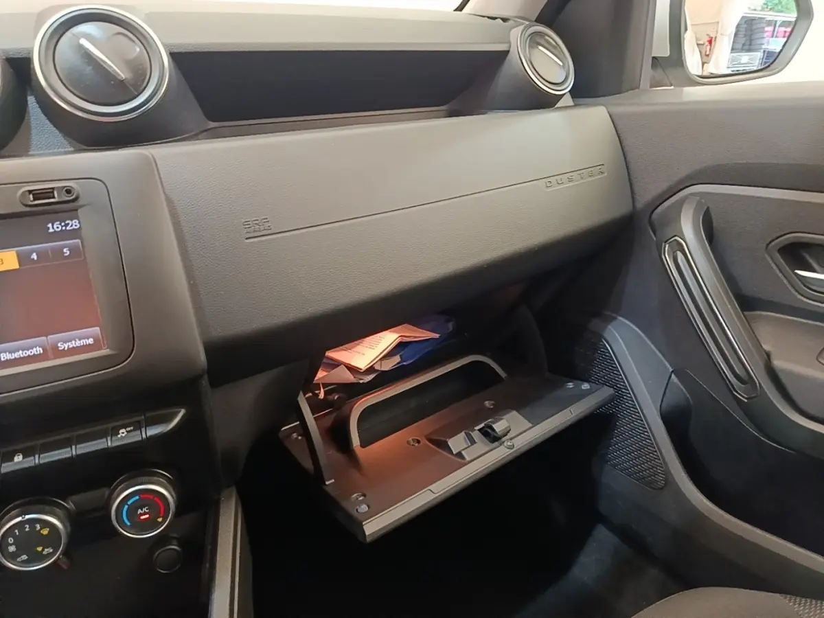 Intérieur côté passager du Dacia Duster 2021, vue sur la boîte à gants ouverte et tableau de bord noir.