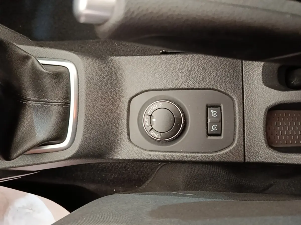 Gros plan sur la molette de sélection 4x4 et les boutons de contrôle sur la console centrale noire du Dacia Duster blanc.