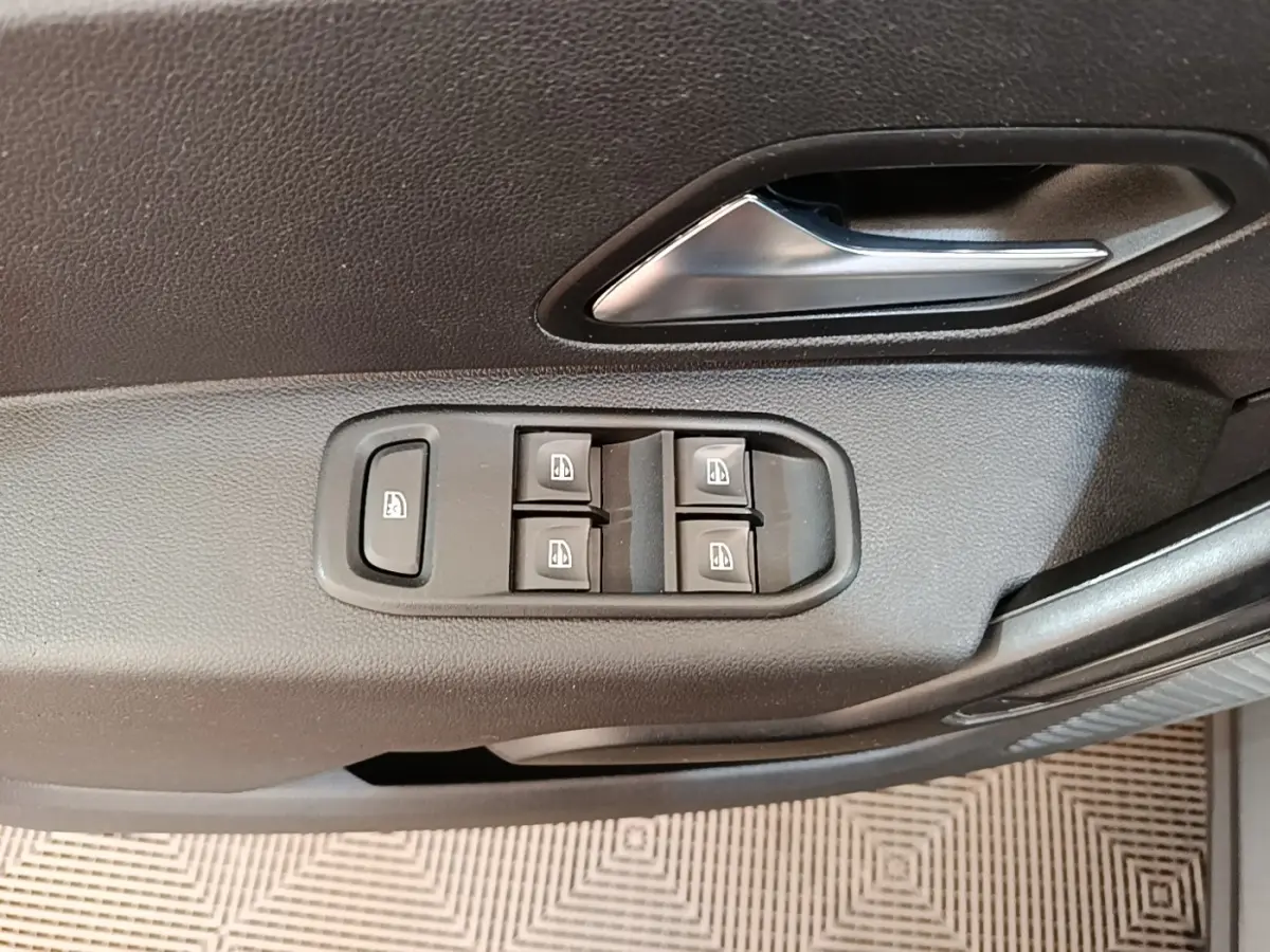 Gros plan sur la commande des vitres électriques et la poignée intérieure côté conducteur du Dacia Duster blanc.