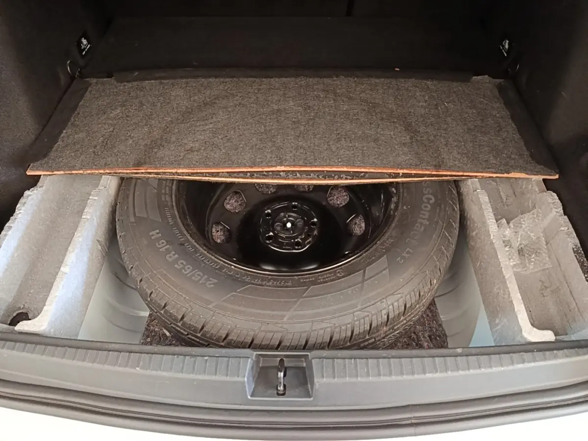 Vue du coffre ouvert d'un Dacia Duster blanc, montrant la roue de secours et le compartiment de rangement sous la tablette.