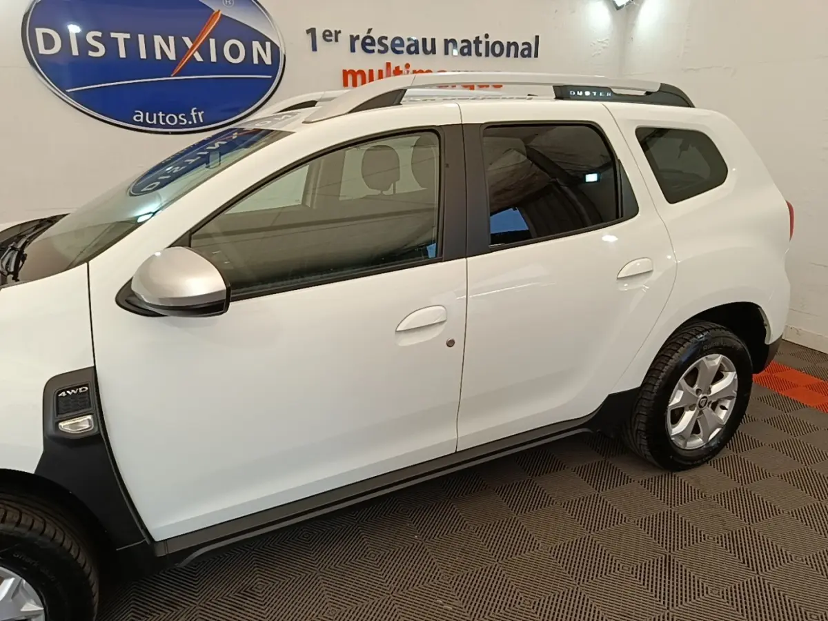 Vue de profil côté gauche du Dacia Duster blanc 2021 avec badge 4x4 et barres de toit noires.