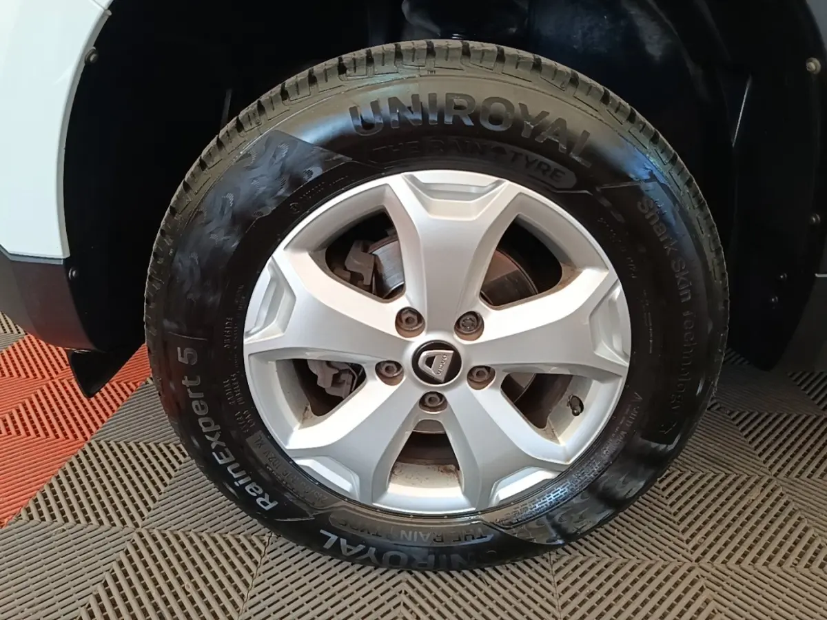 Gros plan sur la roue avant gauche d'un Dacia Duster blanc avec jante argentée et pneu Uniroyal RainExpert 5.