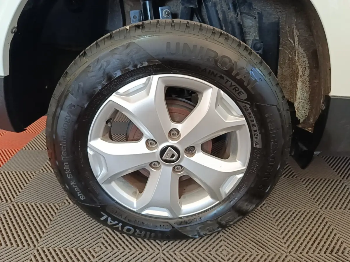 Gros plan sur la roue avant gauche du Dacia Duster blanc, mettant en valeur la jante argentée et le pneu Uniroyal.