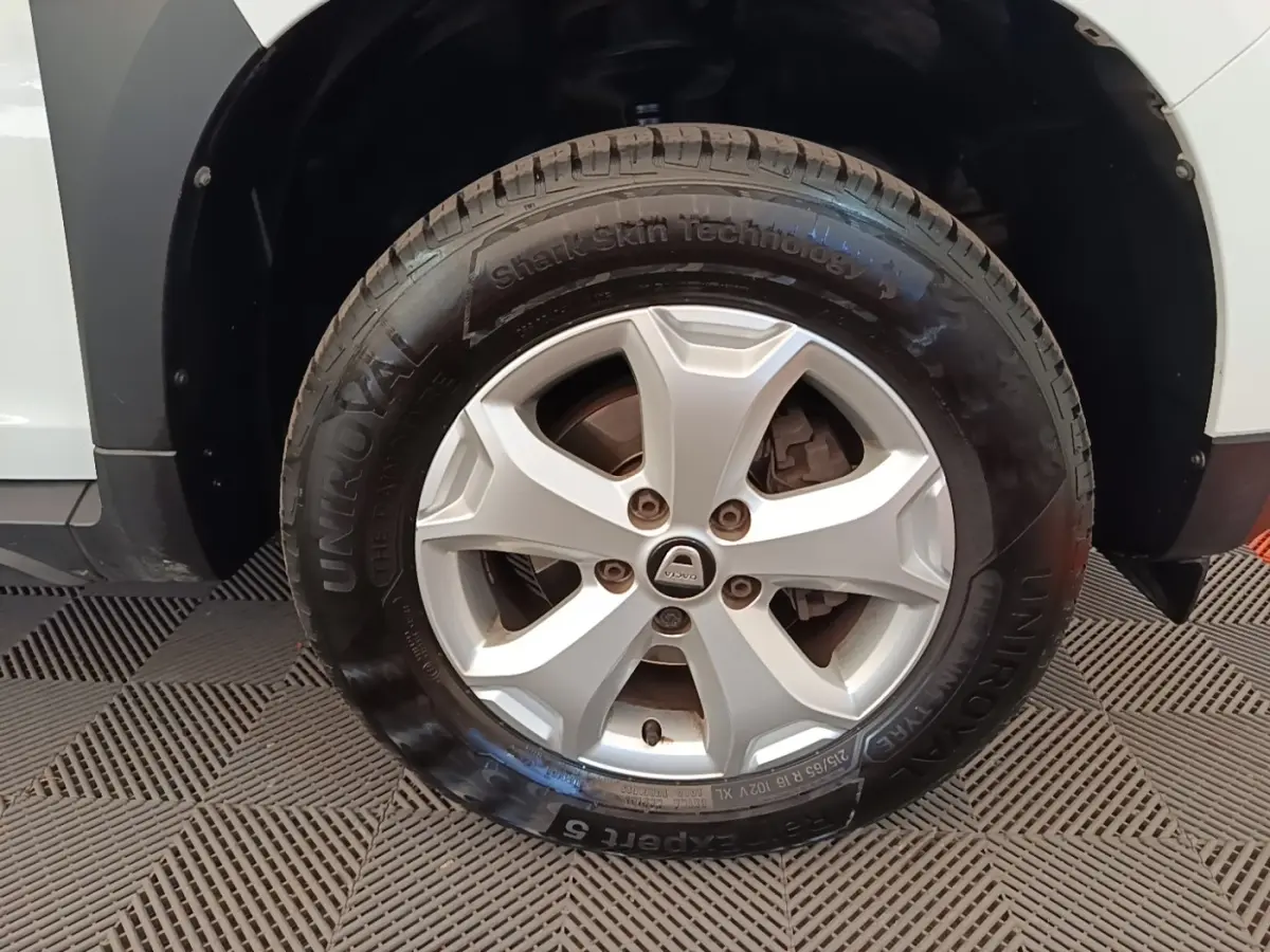 Gros plan sur la roue avant droite d’un Dacia Duster blanc, mettant en valeur la jante argentée et le pneu Uniroyal.