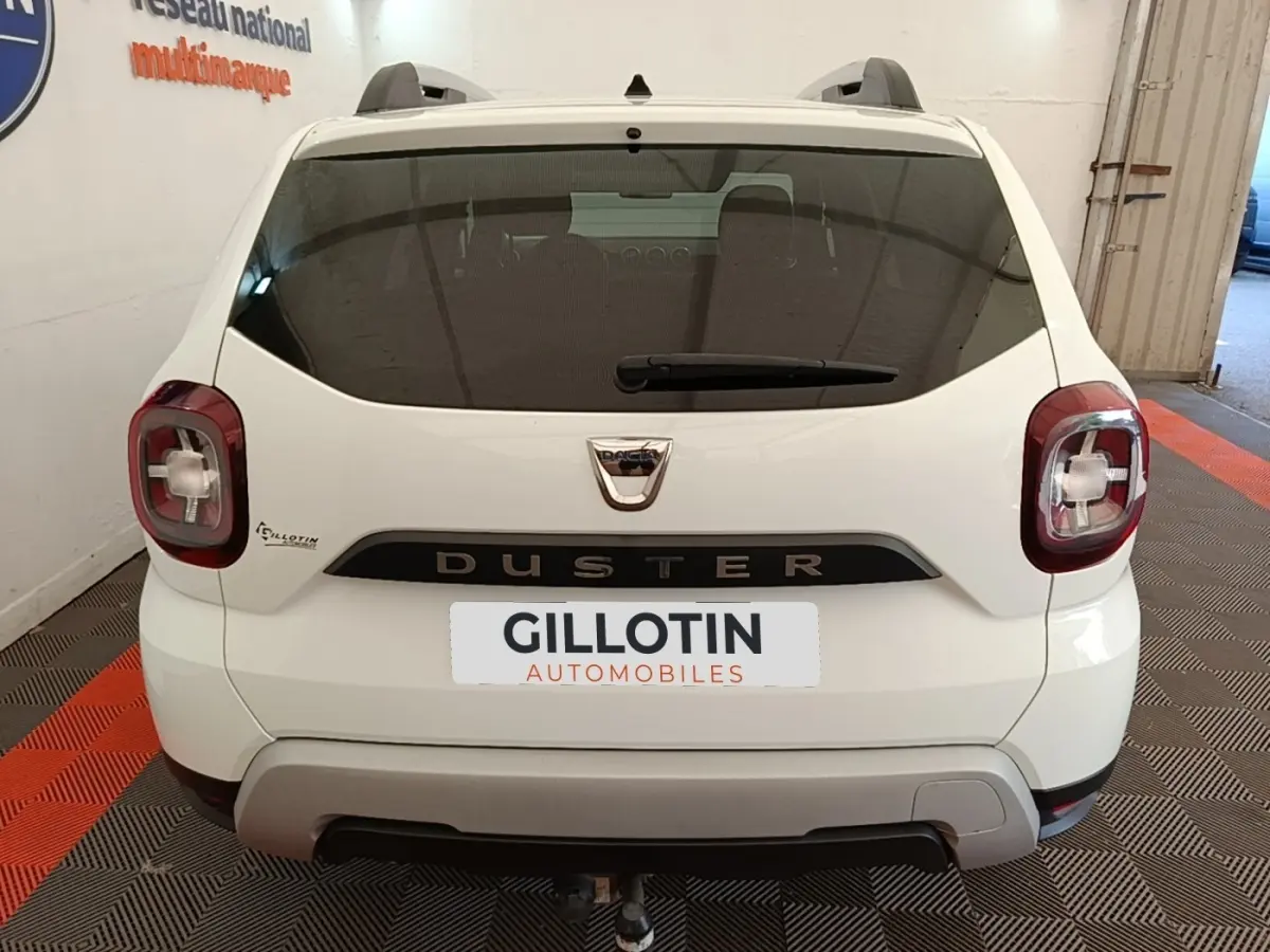 Vue arrière d'un Dacia Duster blanc 2021 avec feux carrés et attelage visible dans un garage.