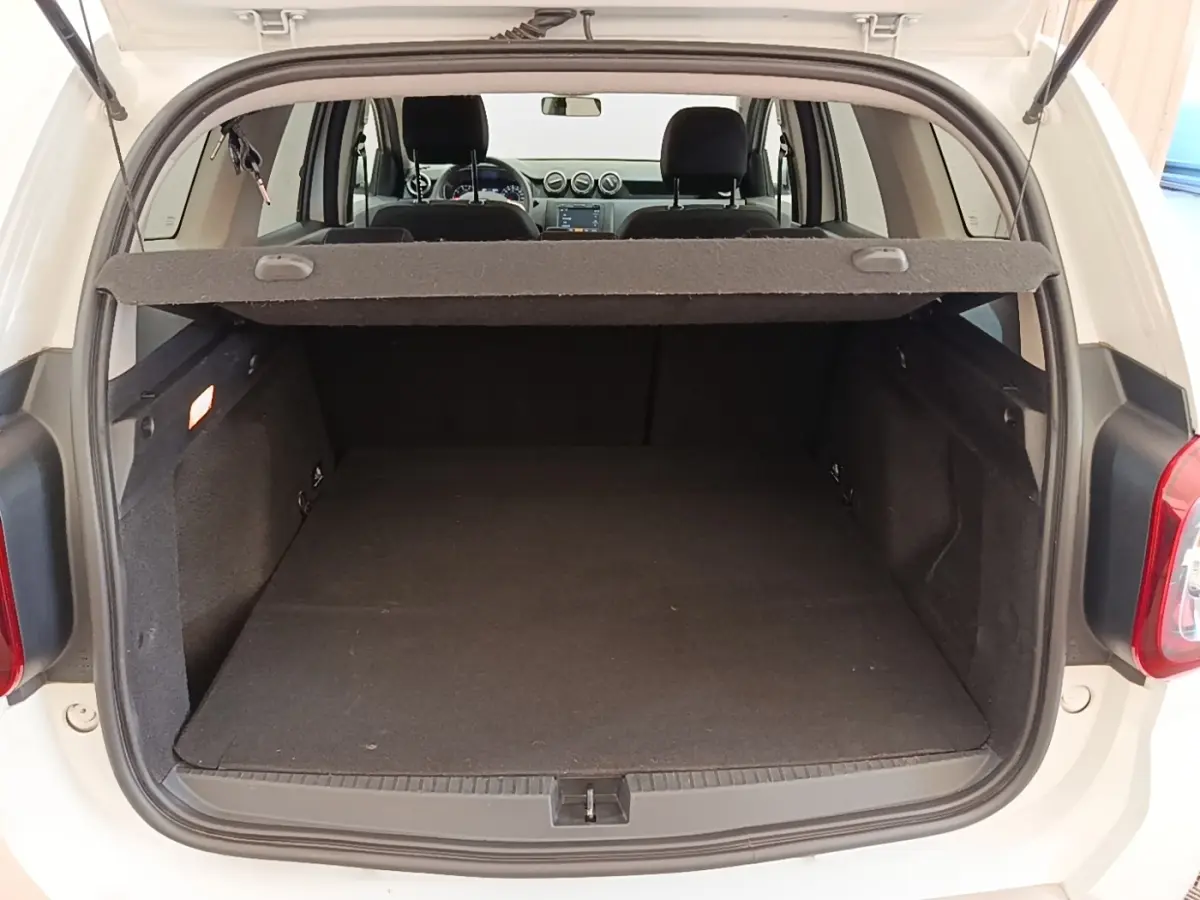 Vue arrière du coffre ouvert d'un Dacia Duster blanc 2021, montrant l'espace de chargement et l'intérieur noir.