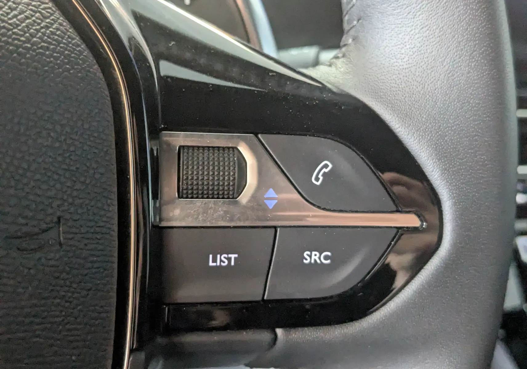 Gros plan sur les commandes gauche du volant noir du Peugeot 2008 Hybrid 145 e-DCS6 Allure, boutons SRC et LIST visibles.