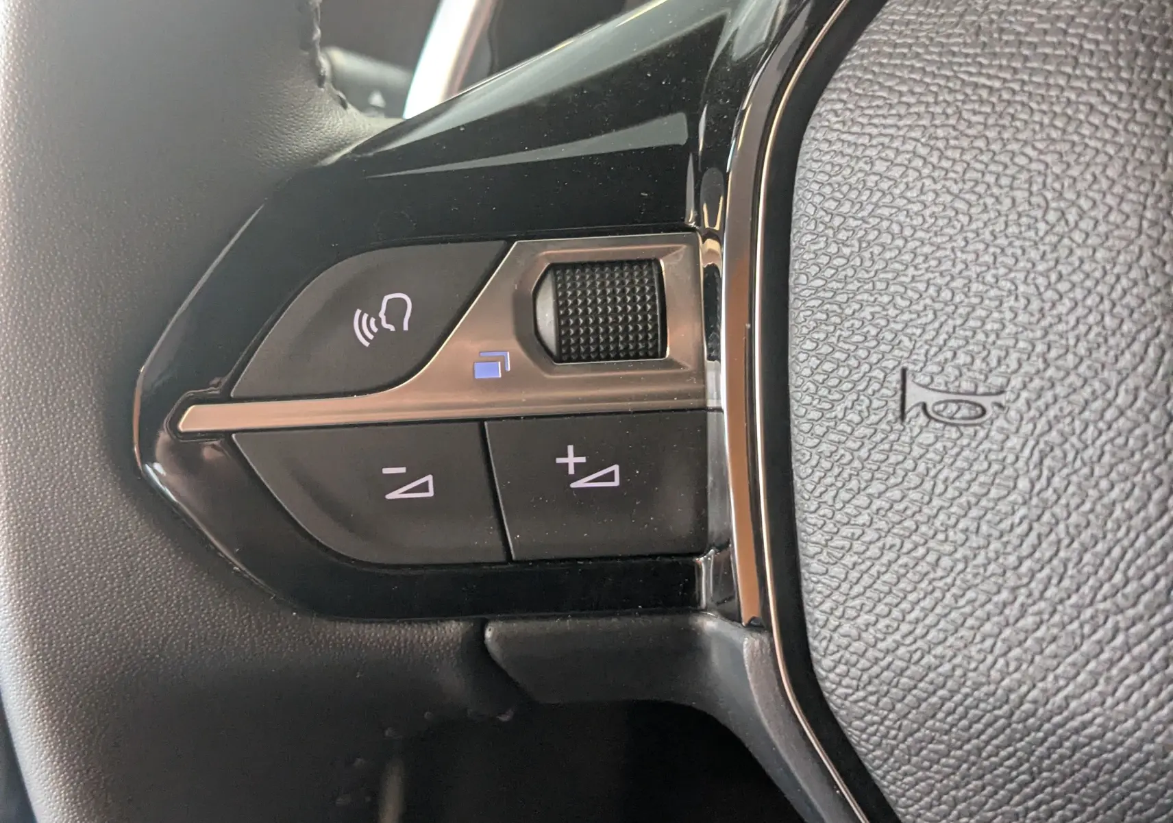 Gros plan sur les commandes de volume au volant noir du Peugeot 2008 Hybrid 145 e-DCS6 Allure, finition tissu gris-noir.