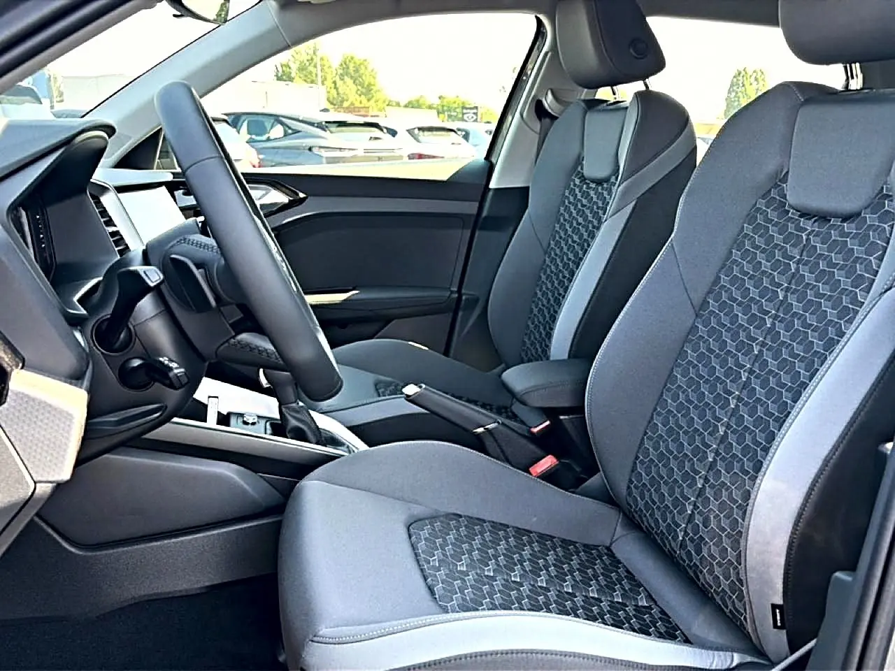 Vue intérieure côté conducteur de l'Audi A1 Sportback 2026, sièges sport gris avec motifs hexagonaux et volant cuir multifonction.