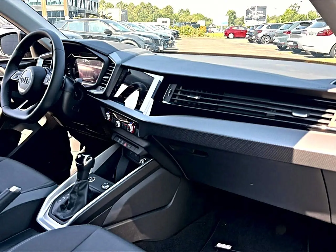 Vue intérieure côté passager de l'Audi A1 Sportback 2026, tableau de bord noir avec écran tactile et volant cuir multifonction.