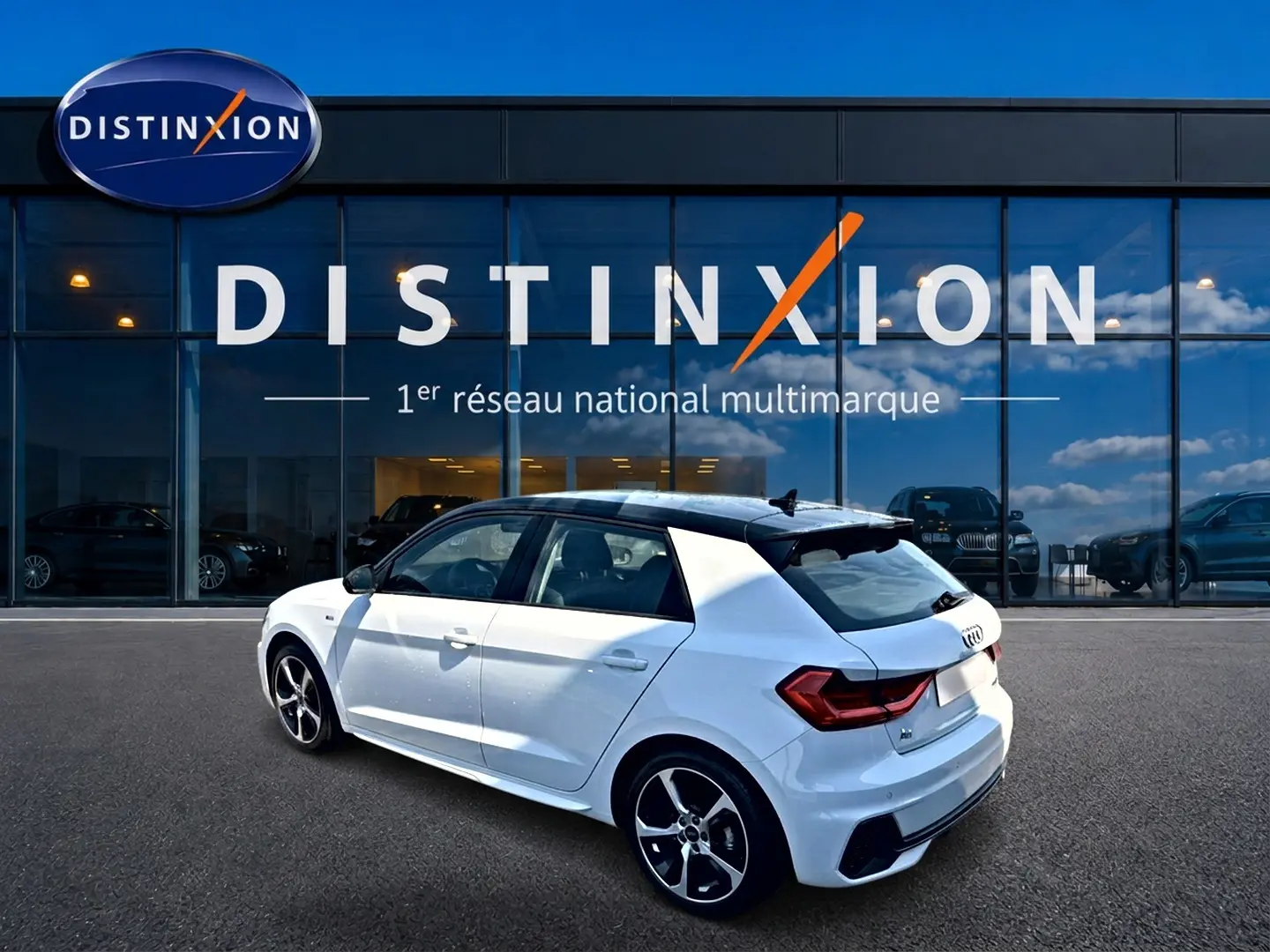 Audi A1 Sportback blanc avec toit noir en 3/4 arrière droit, jantes alu et becquet arrière visible devant showroom Distinxion.