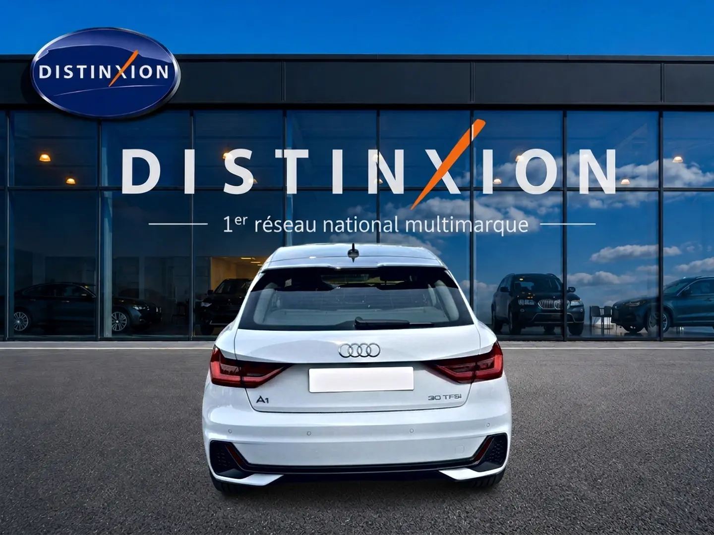 Vue arrière d'une Audi A1 Sportback blanche avec feux LED et becquet, stationnée devant une vitrine Distinxion.