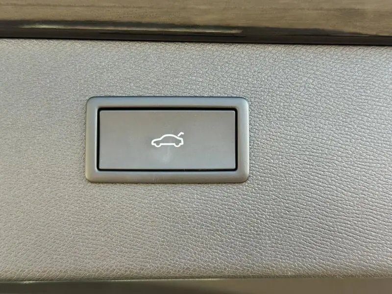 Bouton intérieur de déverrouillage du coffre sur CUPRA Formentor 1.5 eTSI Hybrid 2025, vue rapprochée sur fond gris texturé.