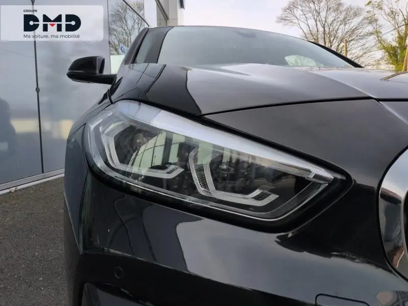 Gros plan sur le phare avant gauche d’une BMW Série 1 118iA 2024 en Saphirschwarz métallisé, avec détails LED distinctifs.