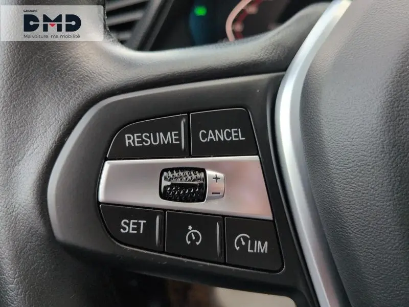 Gros plan sur les commandes du régulateur de vitesse au volant cuir d'une BMW Série 1 118iA Saphirschwarz 2024.