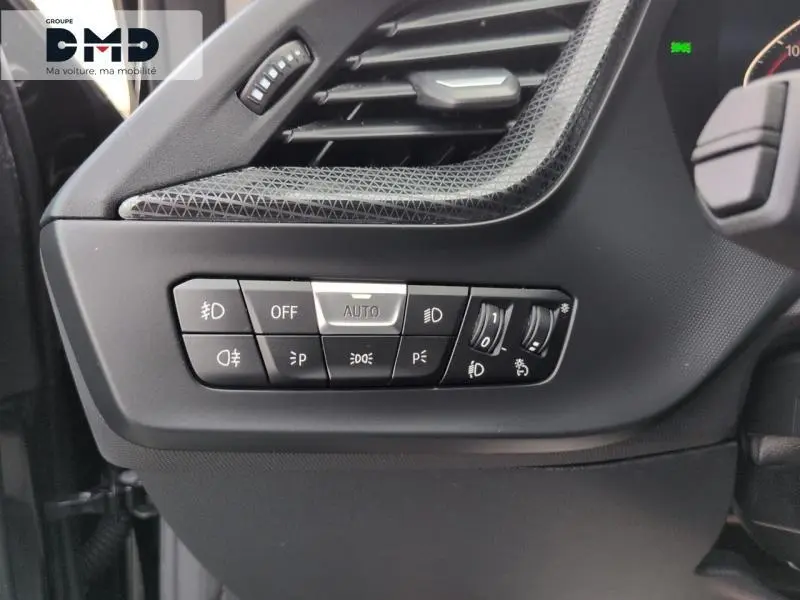 Gros plan sur les commandes d'éclairage à gauche du volant dans une BMW Série 1 118iA 2024 couleur Saphirschwarz métallisé.