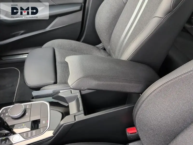 Vue rapprochée de l'accoudoir central noir et des sièges sport gris avec bandes claires dans une BMW Série 1 118iA 2024.