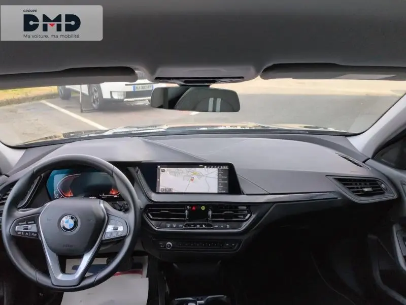 Vue intérieure avant de la BMW Série 1 118iA 2024, tableau de bord noir avec écran tactile GPS et volant multifonction cuir.