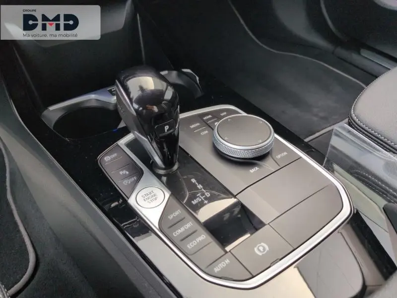 Gros plan sur la console centrale noire brillante de la BMW Série 1 118iA 2024 avec levier de vitesse automatique et commandes de mode de conduite.