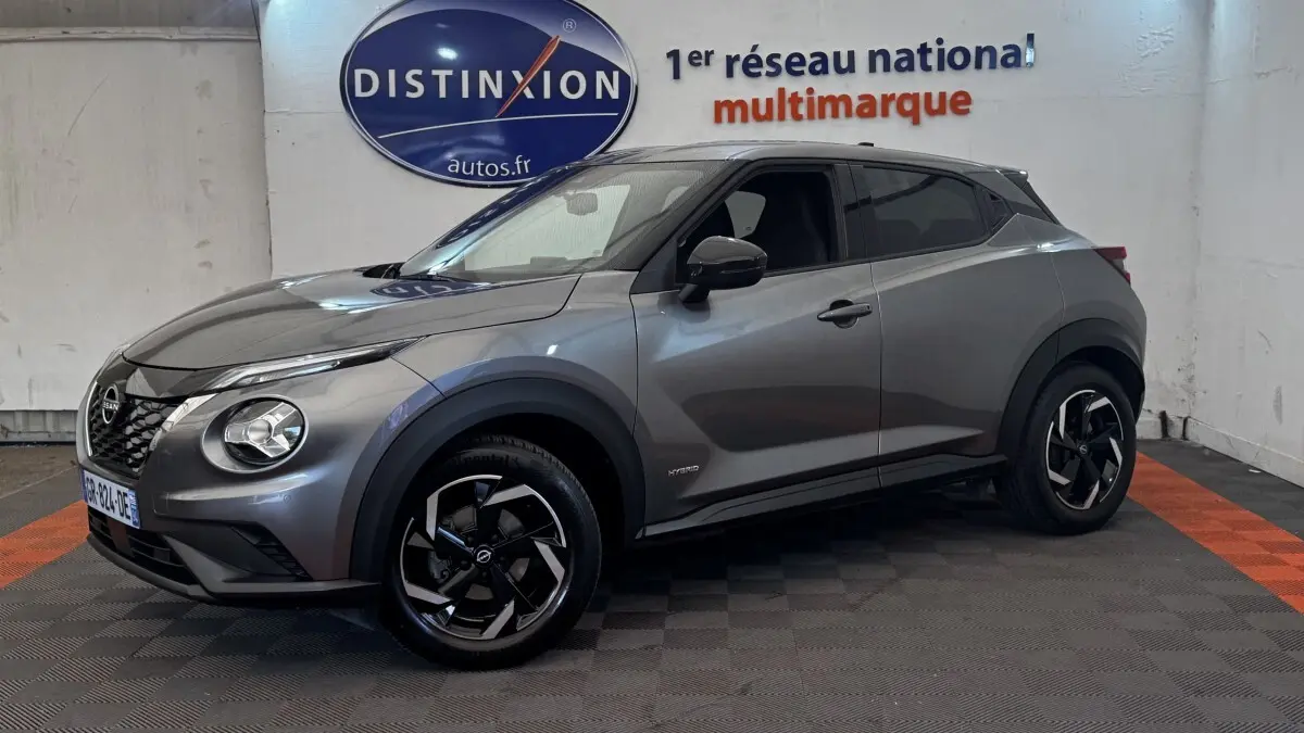 Nissan Juke Hybrid gris foncé vu de profil droit en intérieur, avec jantes noires et détails hybrides visibles.