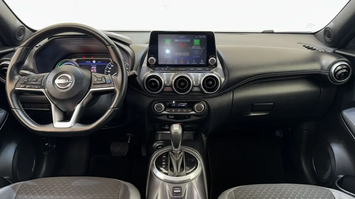 Vue intérieure frontale du tableau de bord noir du Nissan Juke Hybrid 143 Business+ avec écran tactile et volant cuir.