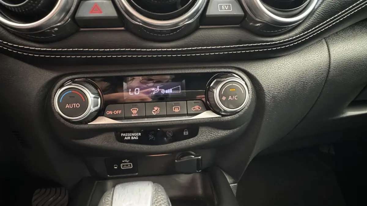 Gros plan sur la console centrale noire du Nissan Juke Hybrid 143 Business+ 2023 avec commandes climatisation et ports USB.