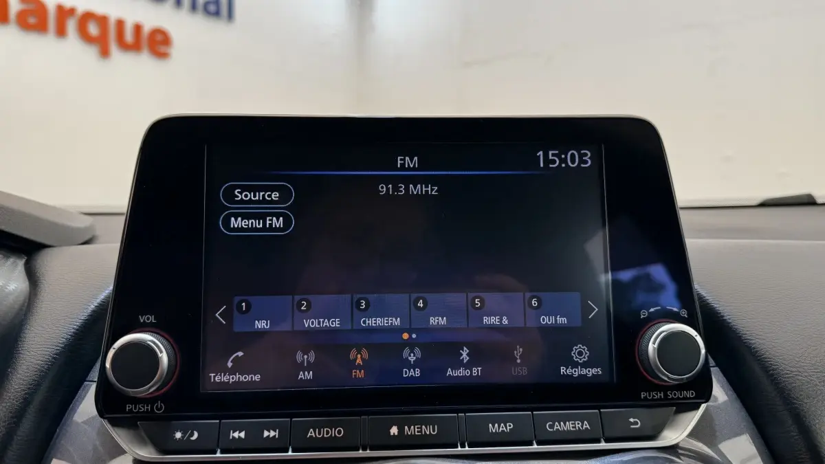 Écran tactile central du Nissan Juke Hybrid 2023 affichant la radio FM avec commandes autour en intérieur noir.