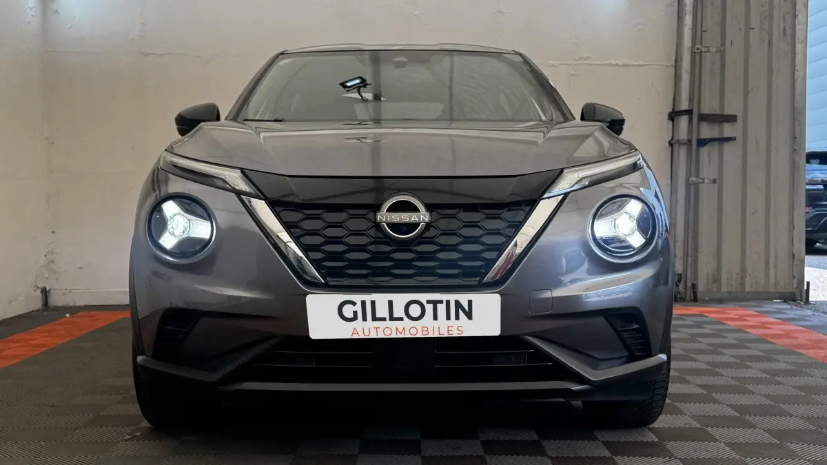 Vue frontale d'un Nissan Juke Hybrid 143 Business+ gris foncé avec phares LED allumés en intérieur.