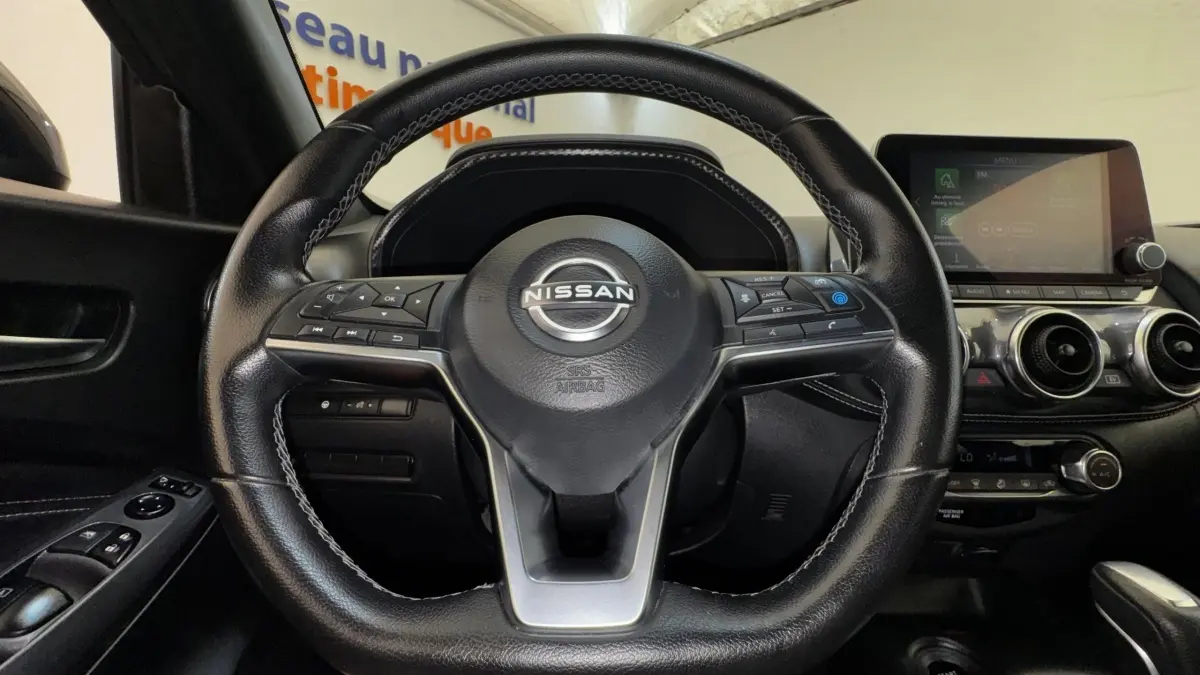 Vue intérieure centrée sur le volant cuir noir du Nissan Juke Hybrid 2023 avec écran tactile et commandes au volant.