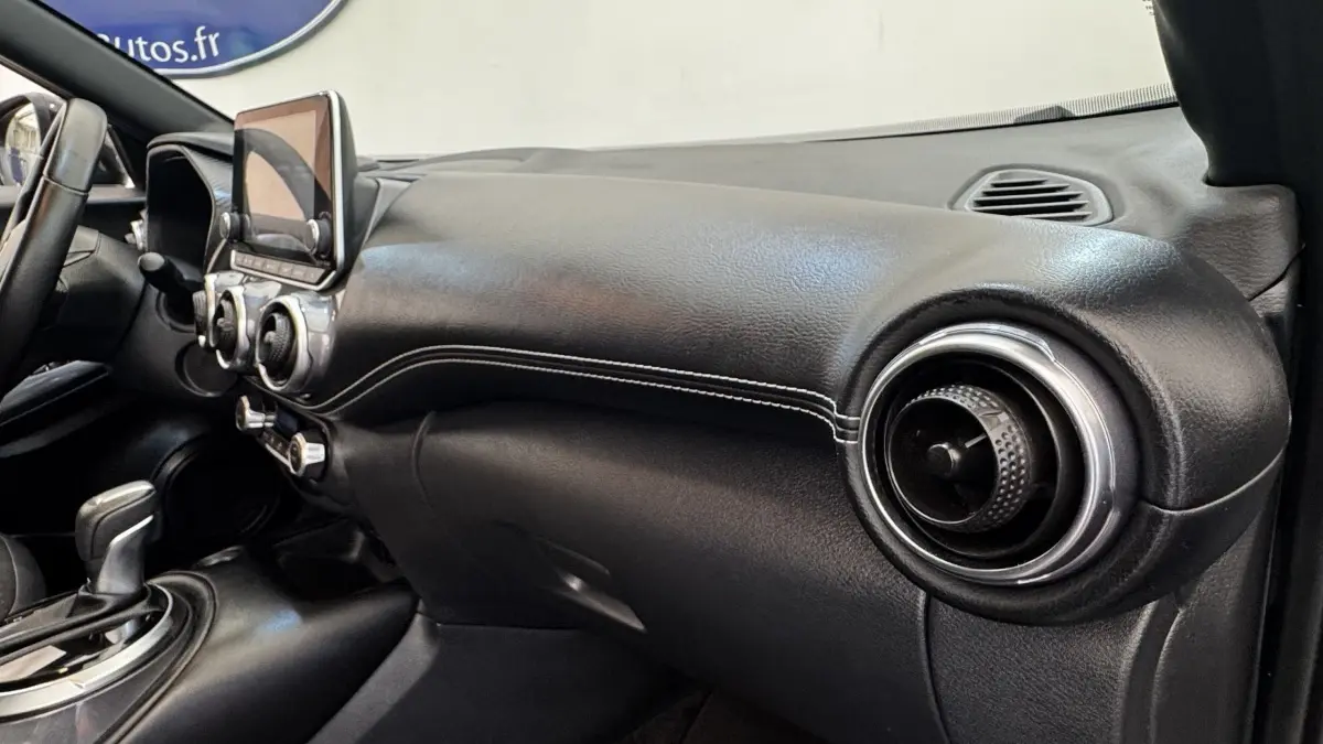 Vue intérieure côté passager du tableau de bord noir avec écran tactile et aérateurs ronds du Nissan Juke Hybrid 2023.