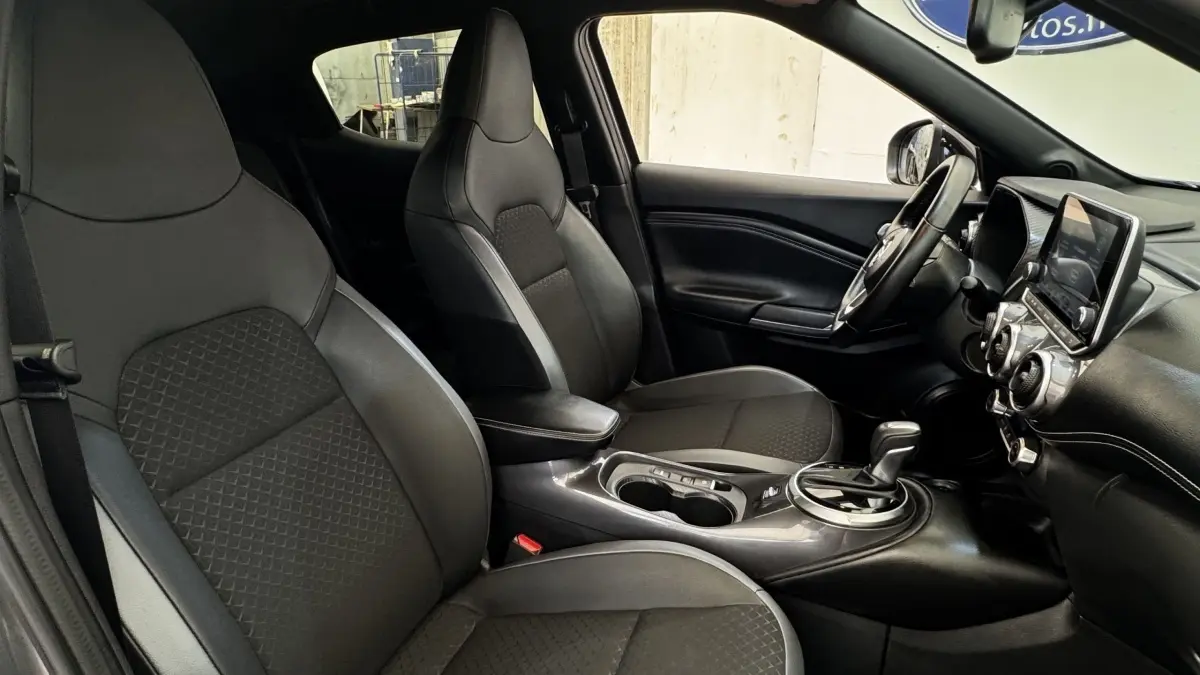 Intérieur avant du Nissan Juke Hybrid 143 Business+ 2023, sièges noirs, console centrale avec boîte auto et écran tactile.