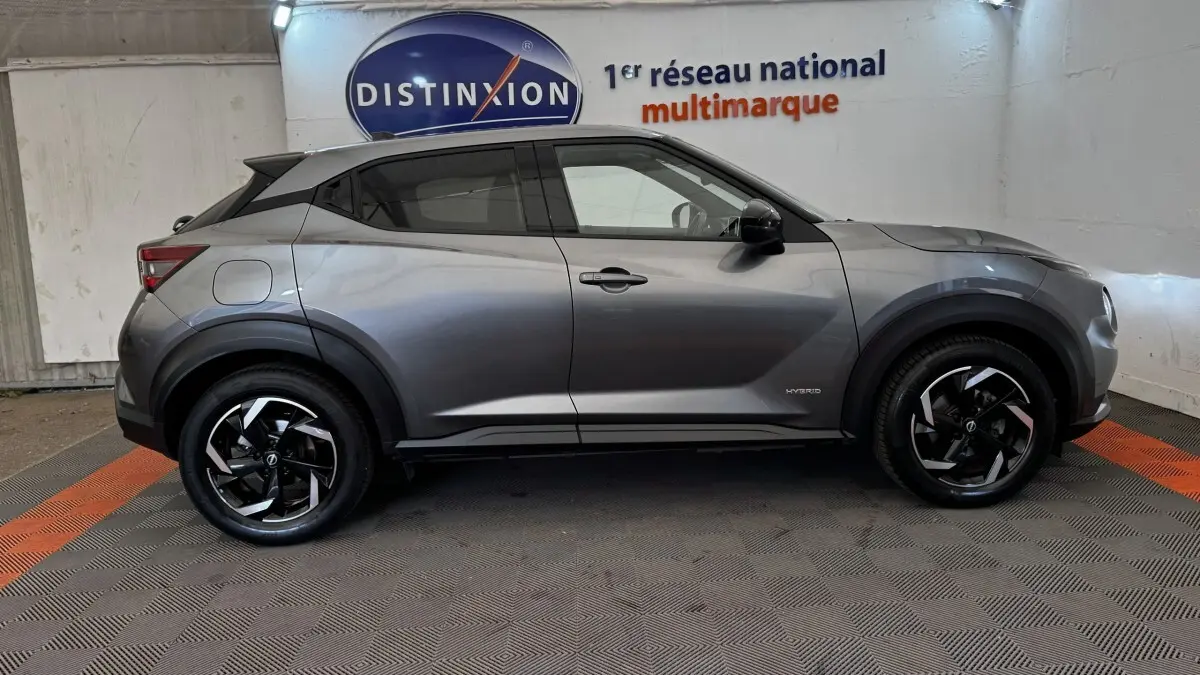 Vue latérale droite d'un Nissan Juke Hybrid 143 Business+ gris foncé avec jantes noires et logo Hybrid visible sur la porte.