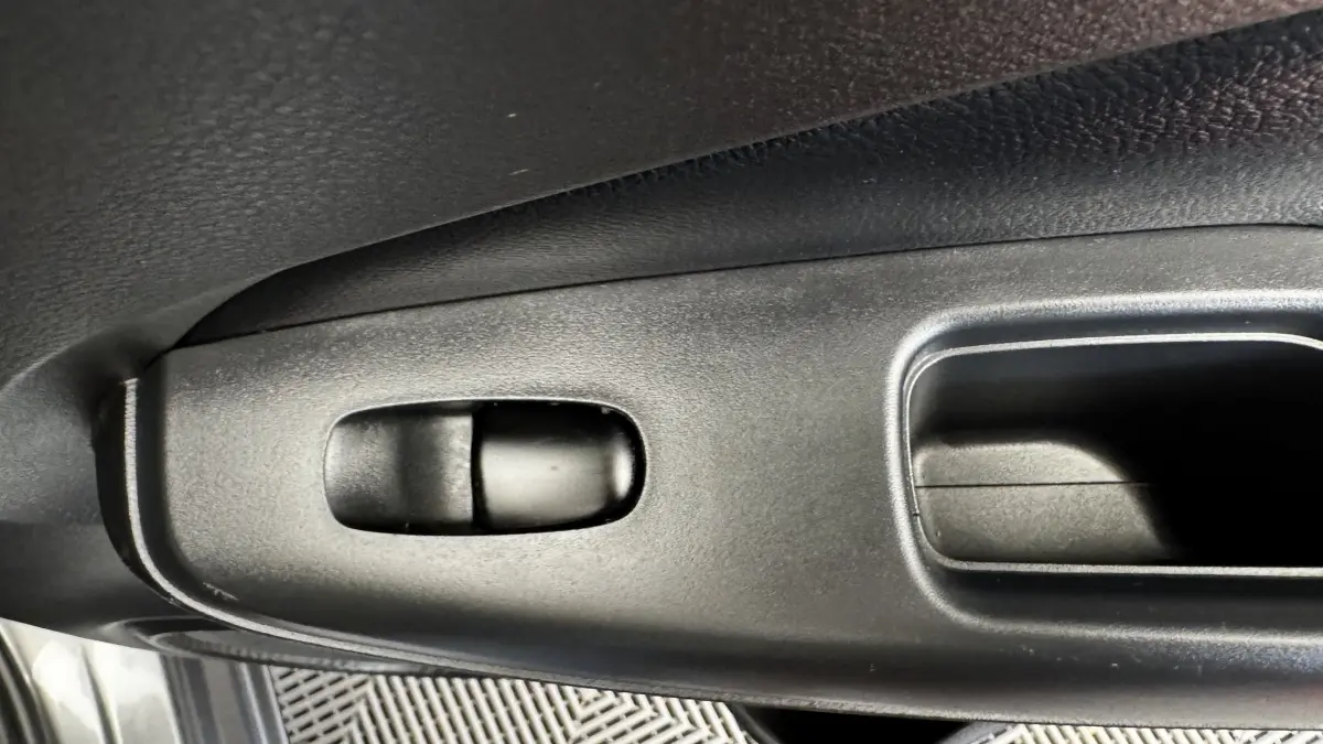 Détail de la commande de lève-vitre côté conducteur en plastique noir dans un Nissan Juke Hybrid 2023 gris foncé.