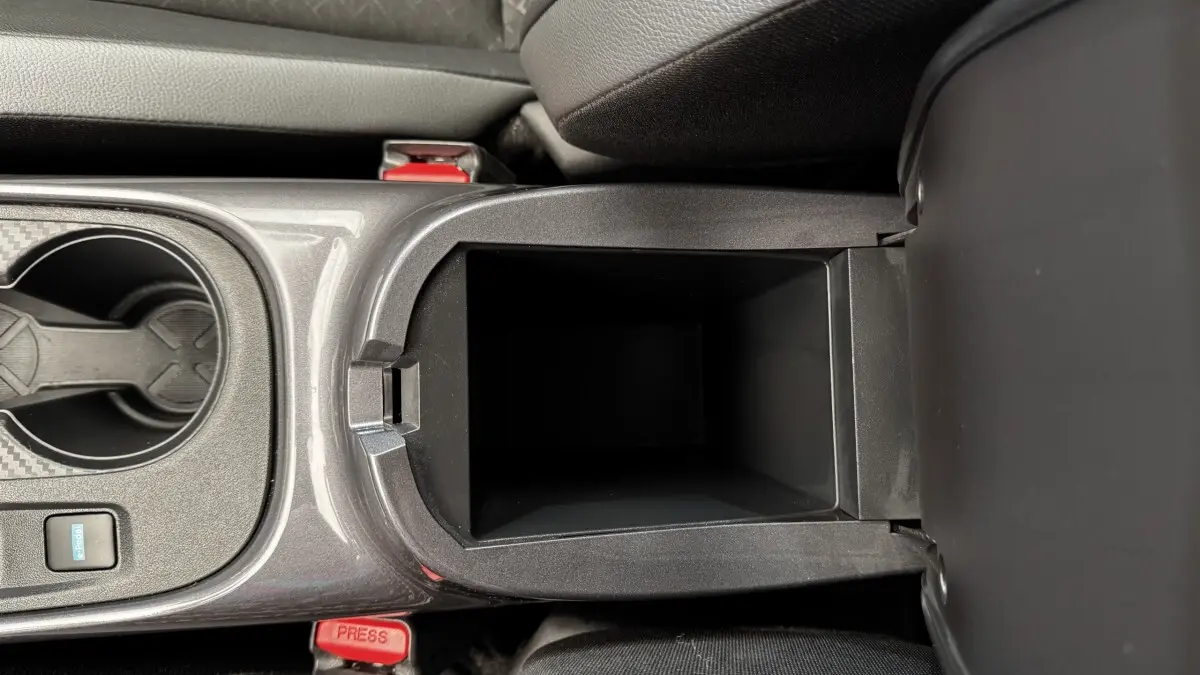 Vue rapprochée de la console centrale ouverte du Nissan Juke Hybrid 143 Business+ gris foncé, montrant le rangement intérieur.