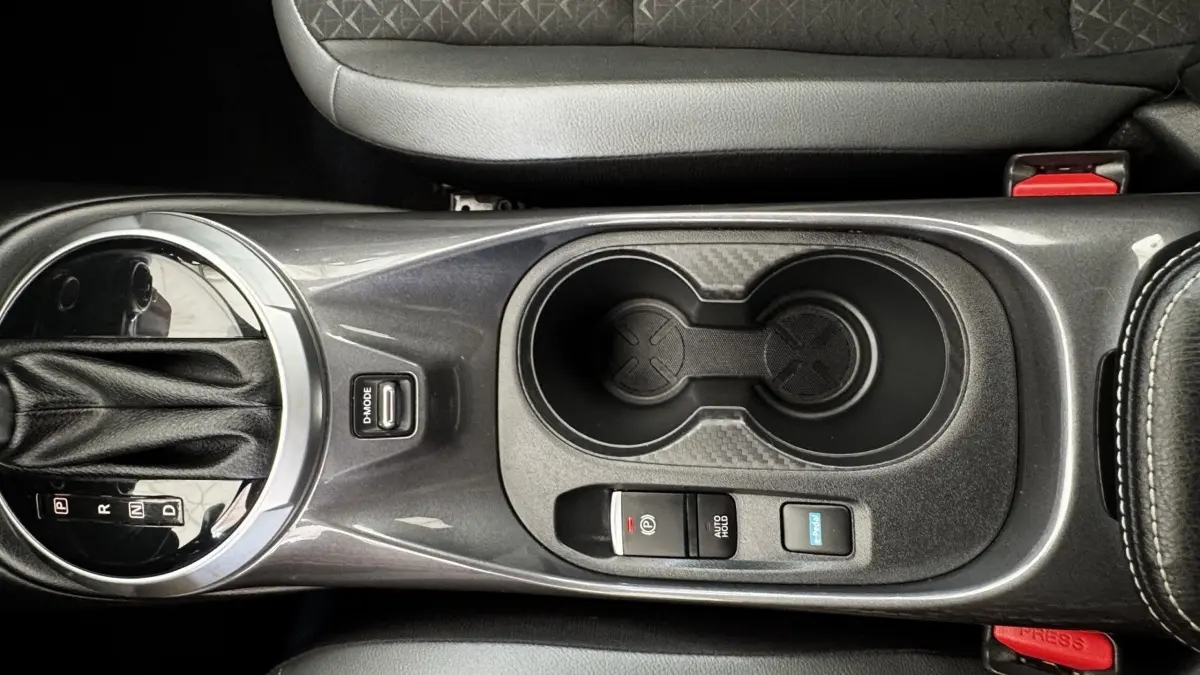 Vue plongeante sur la console centrale grise du Nissan Juke Hybrid 143 Business+ avec levier de vitesses et porte-gobelets.