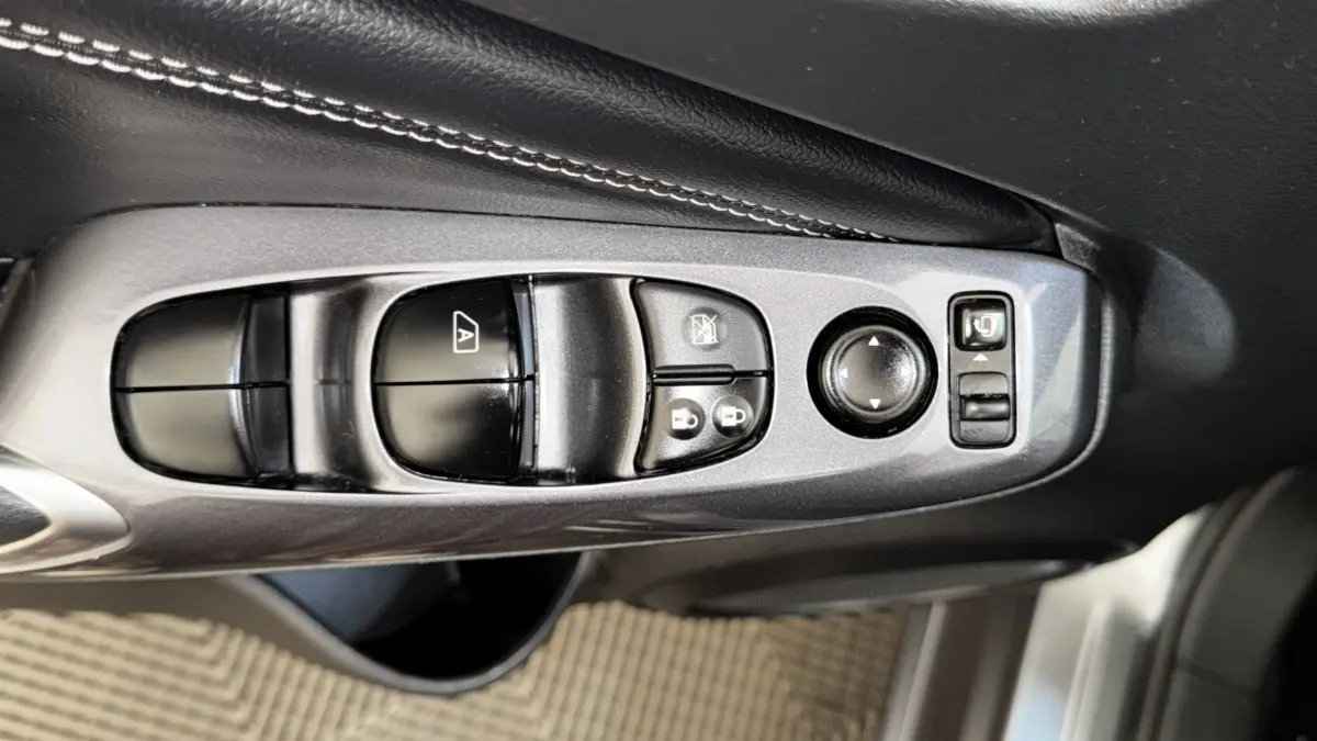 Gros plan sur les commandes de réglage des vitres et rétroviseurs côté conducteur du Nissan Juke Hybrid 143 Business+ gris foncé.