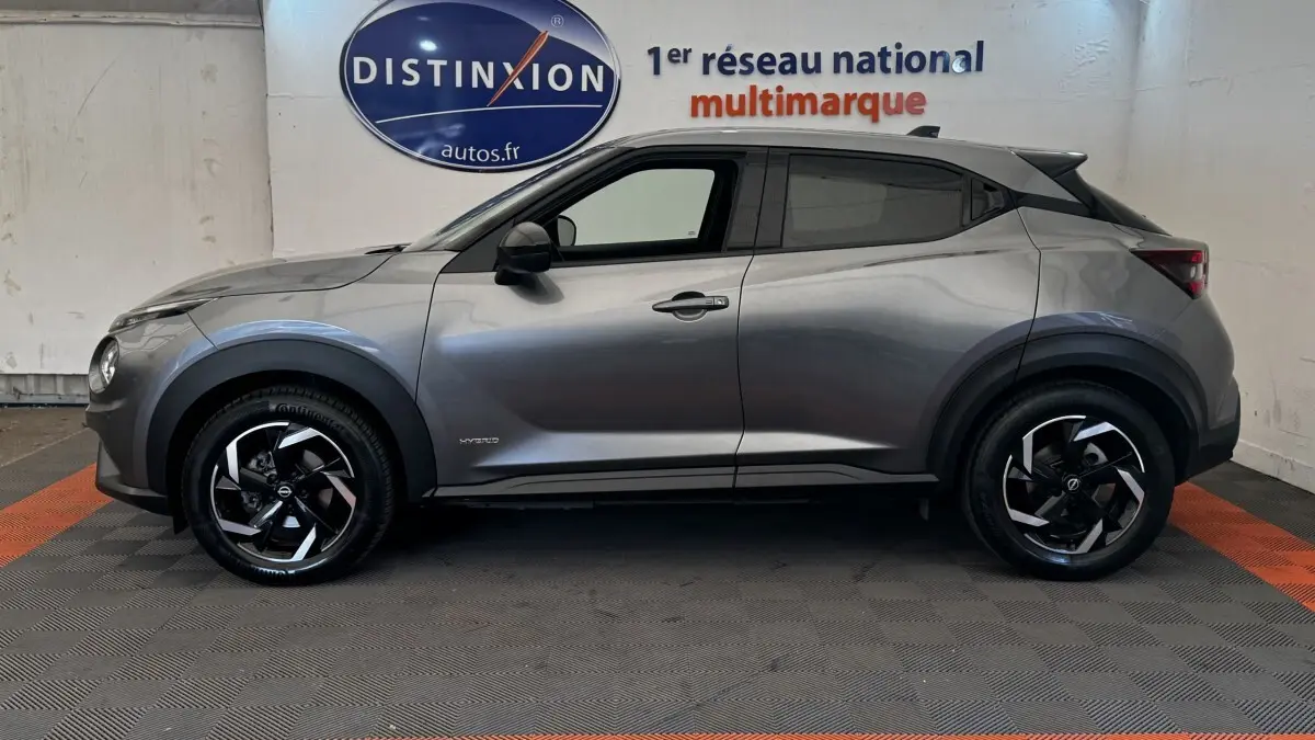 Profil latéral droit du Nissan Juke Hybrid 143 Business+ gris foncé avec jantes noires et logo hybride visible.
