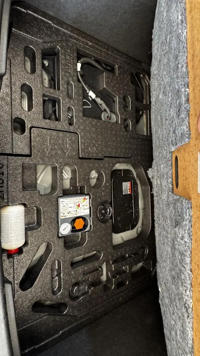 Vue rapprochée du compartiment de rangement sous le plancher du coffre du Nissan Juke Hybrid 143 Business+ gris foncé.