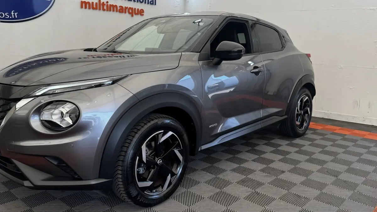 Nissan Juke Hybrid gris foncé vu de 3/4 avant droit, avec jantes noires et logo Hybrid sur la portière.