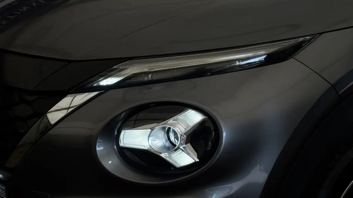 Gros plan sur le phare avant droit et le feu diurne d'un Nissan Juke Hybrid gris foncé, détails modernes et lisses.