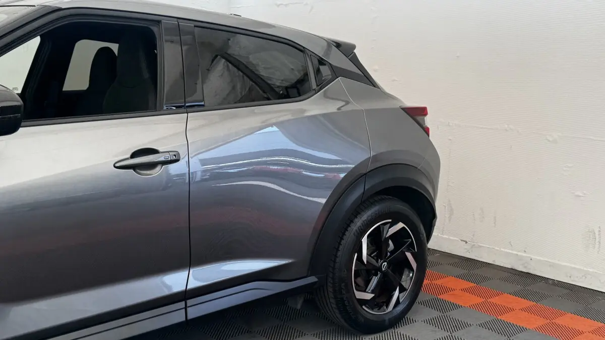 Vue côté droit arrière du Nissan Juke Hybrid 143 Business+ gris foncé avec jante noire et détails de carrosserie marqués.
