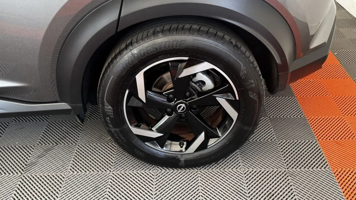 Gros plan sur la roue avant droite du Nissan Juke Hybrid gris foncé avec jante noire et argentée au design moderne.
