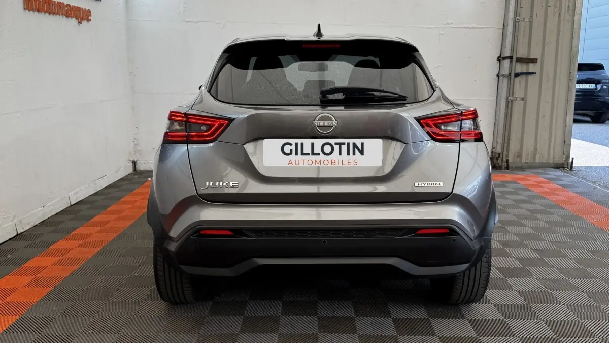 Vue arrière d'un Nissan Juke Hybrid gris foncé 2023 avec feux LED et logo Hybrid visible sur un sol à damiers noir et orange.