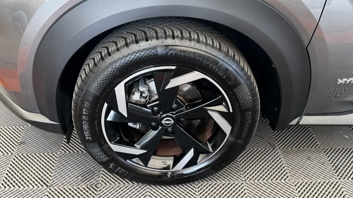Gros plan sur la roue avant droite du Nissan Juke Hybrid gris foncé, avec jante noire et argentée au design géométrique.