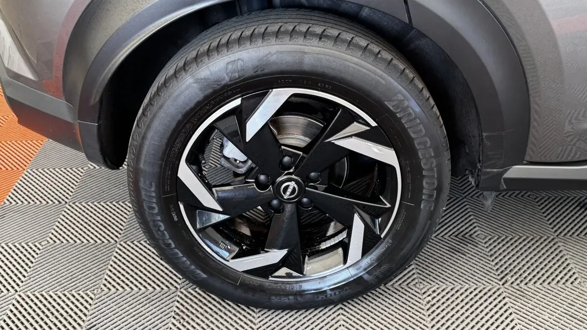 Gros plan sur la roue avant gauche du Nissan Juke Hybrid 143 Business+ gris foncé, jante alliage noire et argentée.