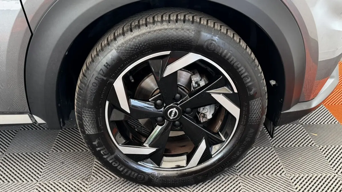 Gros plan sur la roue avant droite du Nissan Juke Hybrid gris foncé, jante alliage noire et argentée au design moderne.