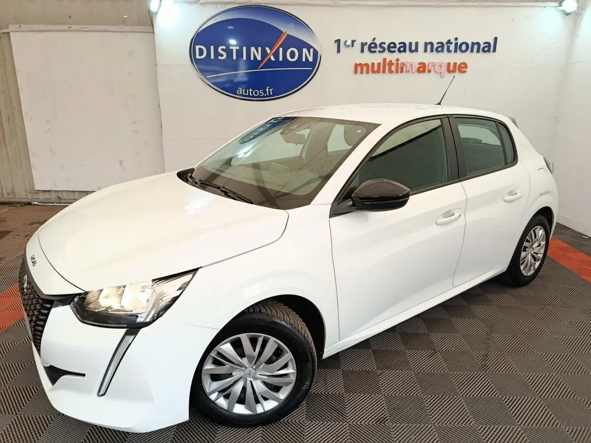 Peugeot 208 blanc vue 3/4 avant droit, phares allumés, rétroviseur noir et jantes alliage visibles.