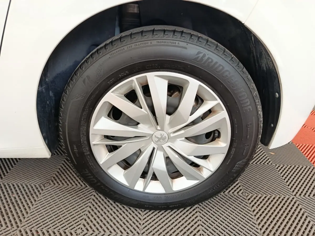 Gros plan sur la roue avant droite d'une Peugeot 208 blanche, avec jante en alliage et pneu Bridgestone.
