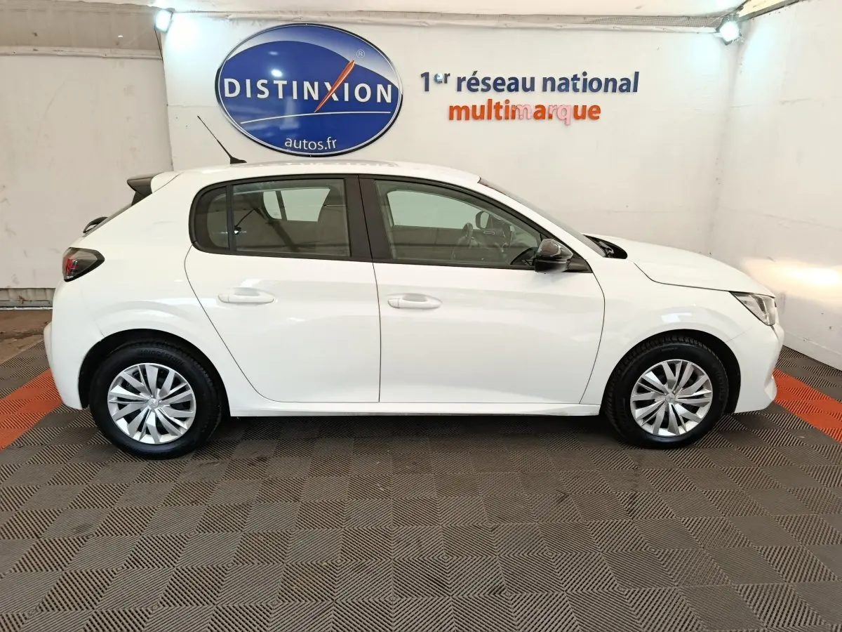 Profil droit d'une Peugeot 208 blanche 2023, version 1.5 BlueHDi Premium, en intérieur sur sol damier gris et orange.