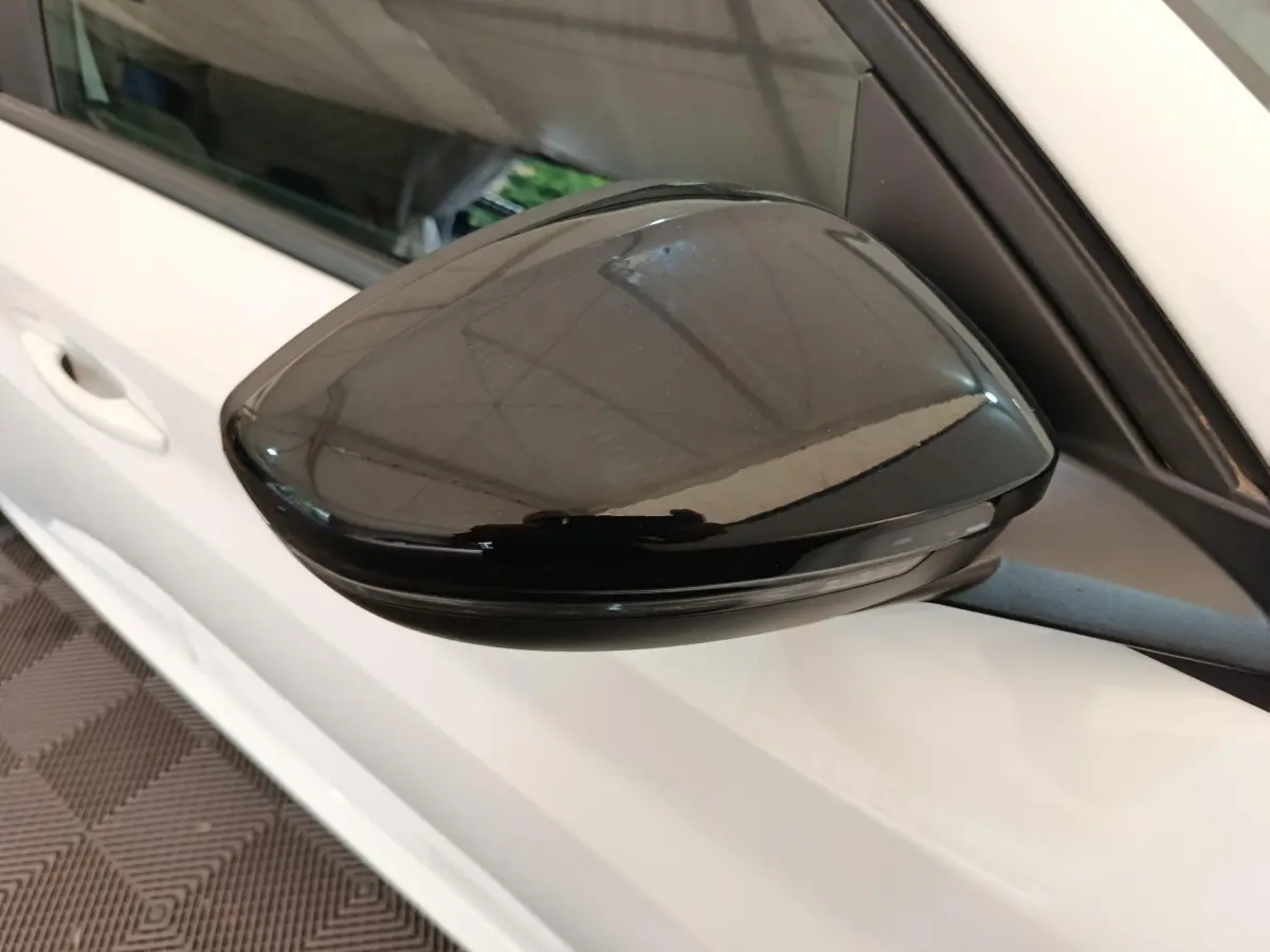 Gros plan sur le rétroviseur noir côté gauche d'une Peugeot 208 blanche, version 1.5 BlueHDi 2023.